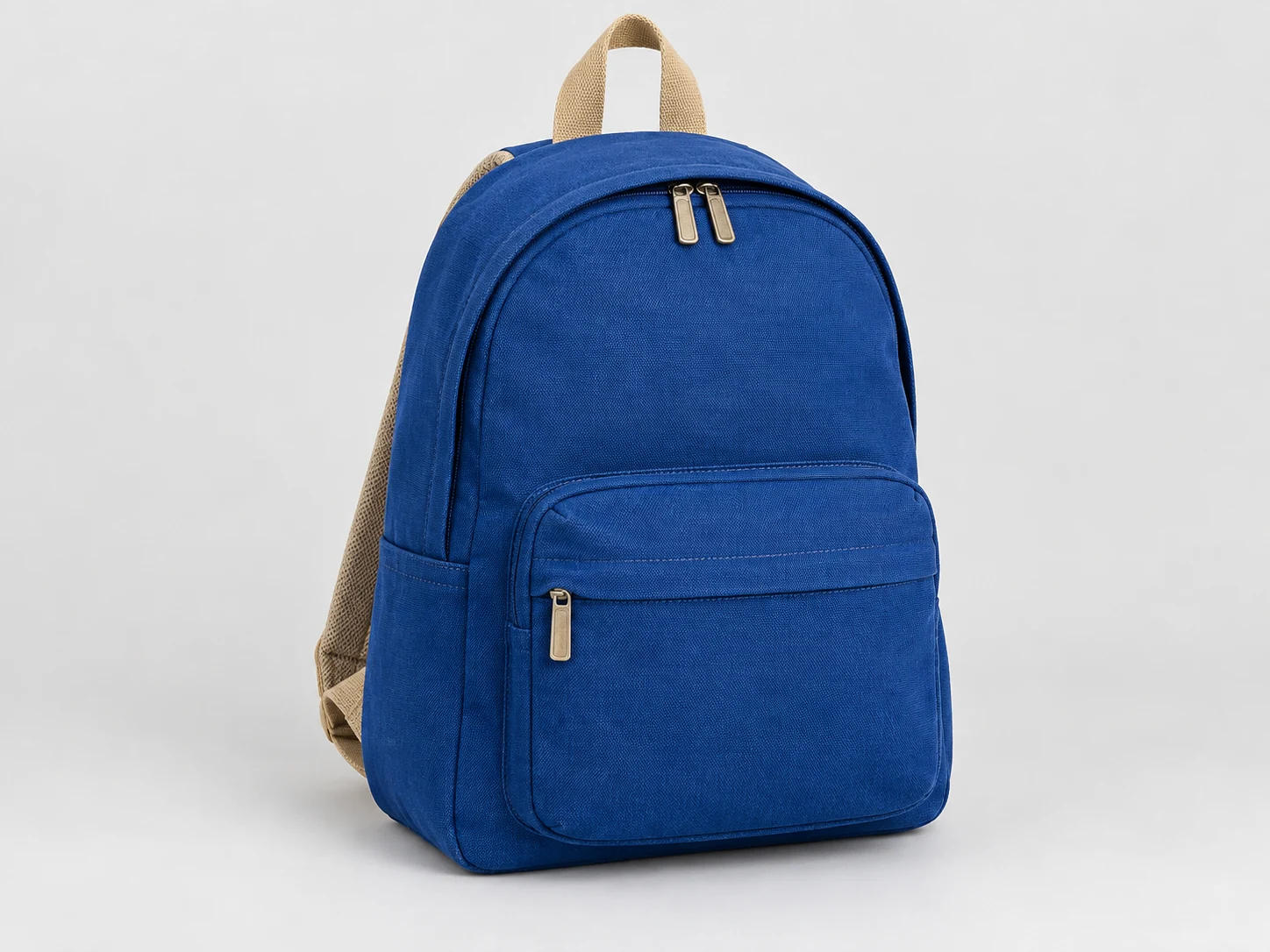 Kobaltblauer Canvas-Rucksack mit sandfarbenen Gurten und metallenen Reißverschlussgriffen vor neutralem hellgrauem Studiohintergrund